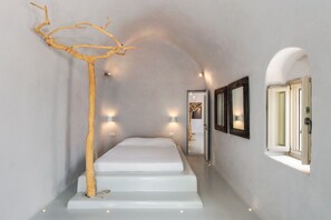 Une chambre à coucher au style minimaliste, avec un lit blanc, une sculpture représentant une branche d’arbre et des lampes fixées au mur.