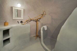 Une salle de bain avec un lavabo blanc, un miroir, une décoration en forme de branche d’arbre et une baignoire.