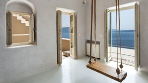 A room with a wooden swing, a staircase, and a view of the sea. - Ammos Oia Mansion (Santorini)
