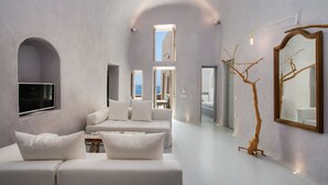 A modern interior with a white sofa, a large mirror, and a unique tree sculpture. - Ammos Oia Mansion (Santorini)