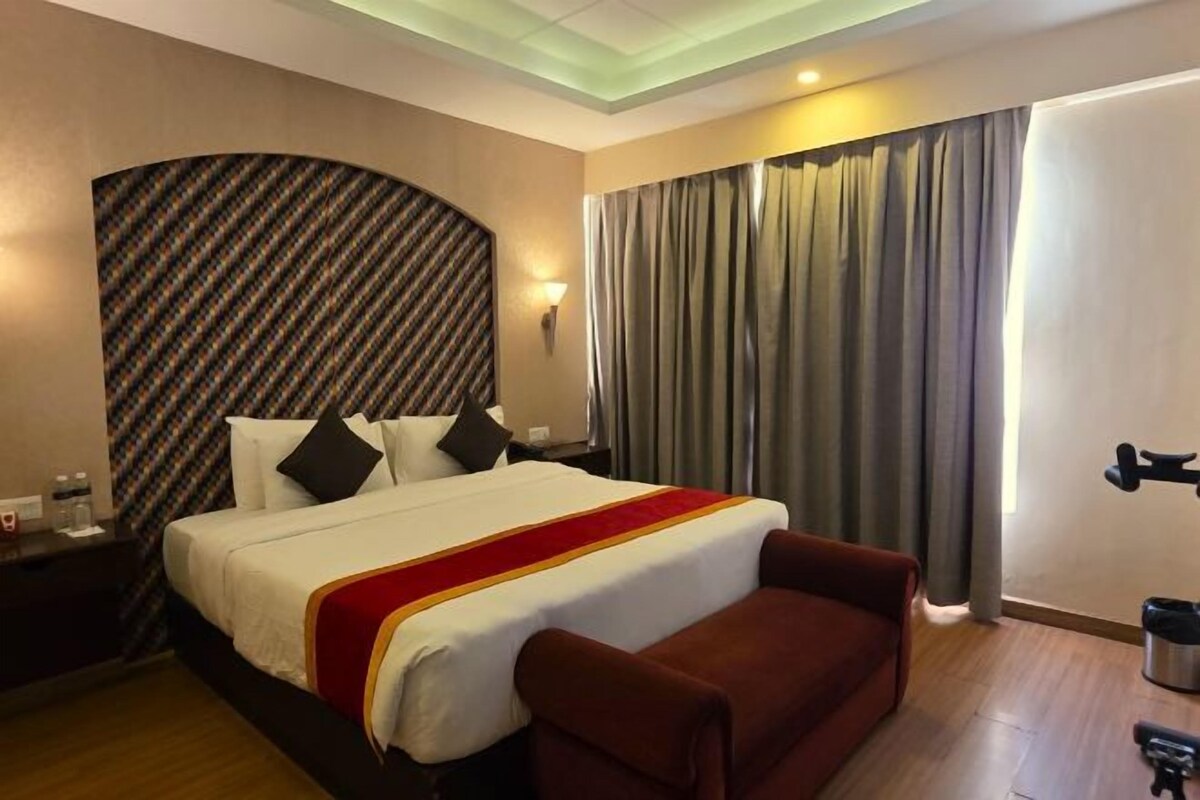 A hotel room with a large bed, a red sofa, a patterned headboard, and a view of the outdoors.