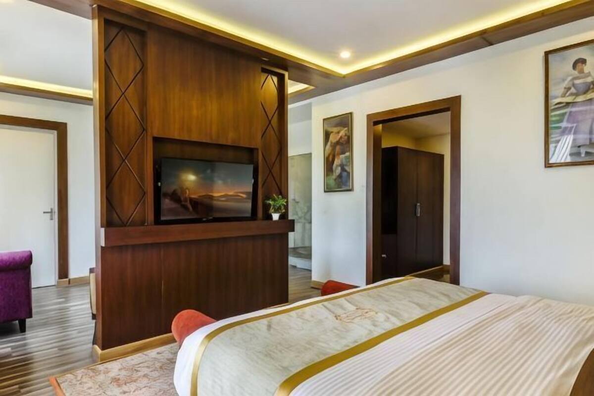 Ein Hotelzimmer mit Bett, Fernseher an einer Holzvertäfelung, einer Tür und einem Bild an der Wand.