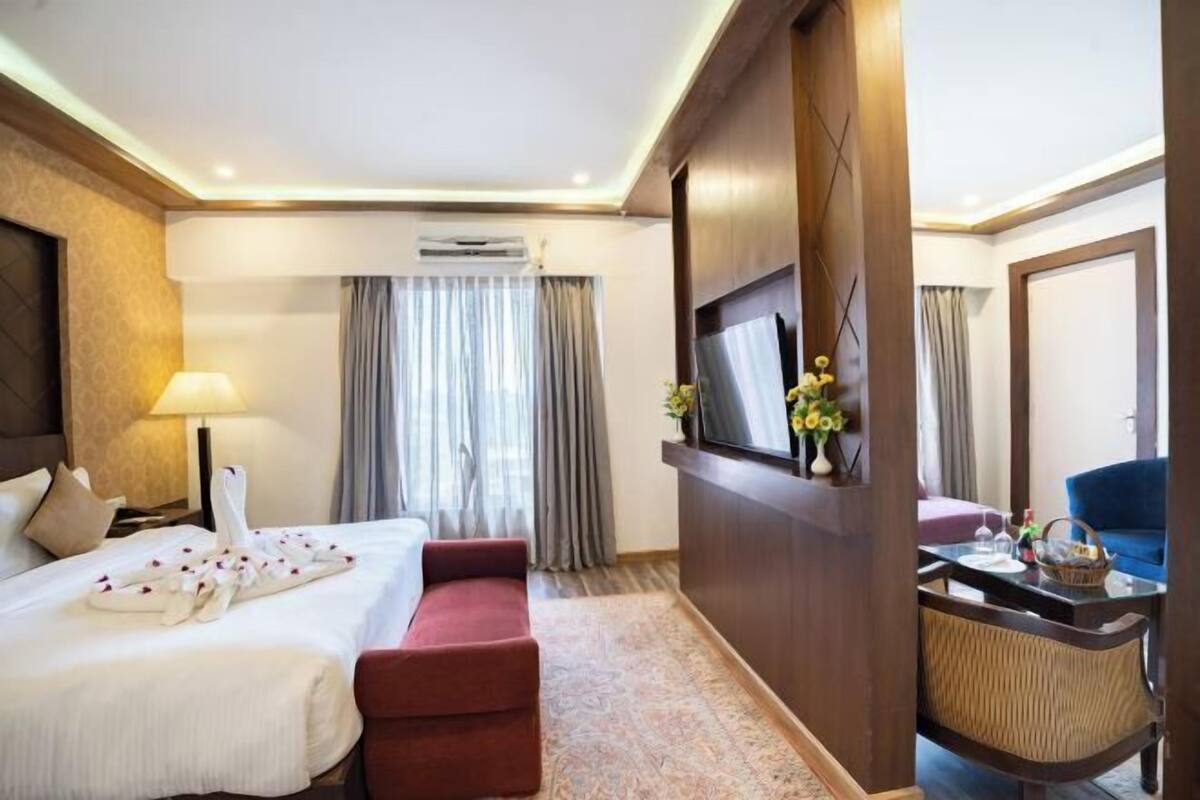 Ein Hotelzimmer mit Bett, Schreibtisch, Sessel, Fernseher und einem fenster mit Vorhängen.