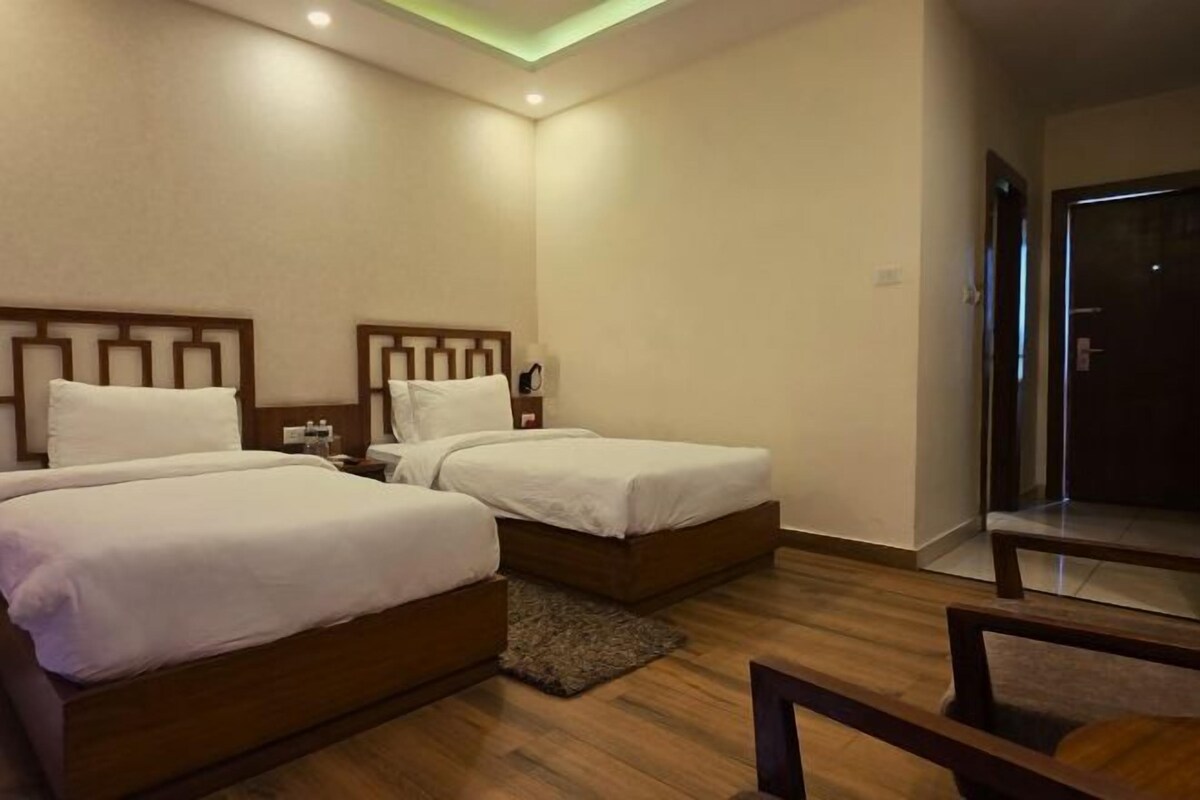 A hotel room with two beds, a wooden floor, a small rug, and a door leading to a balcony.