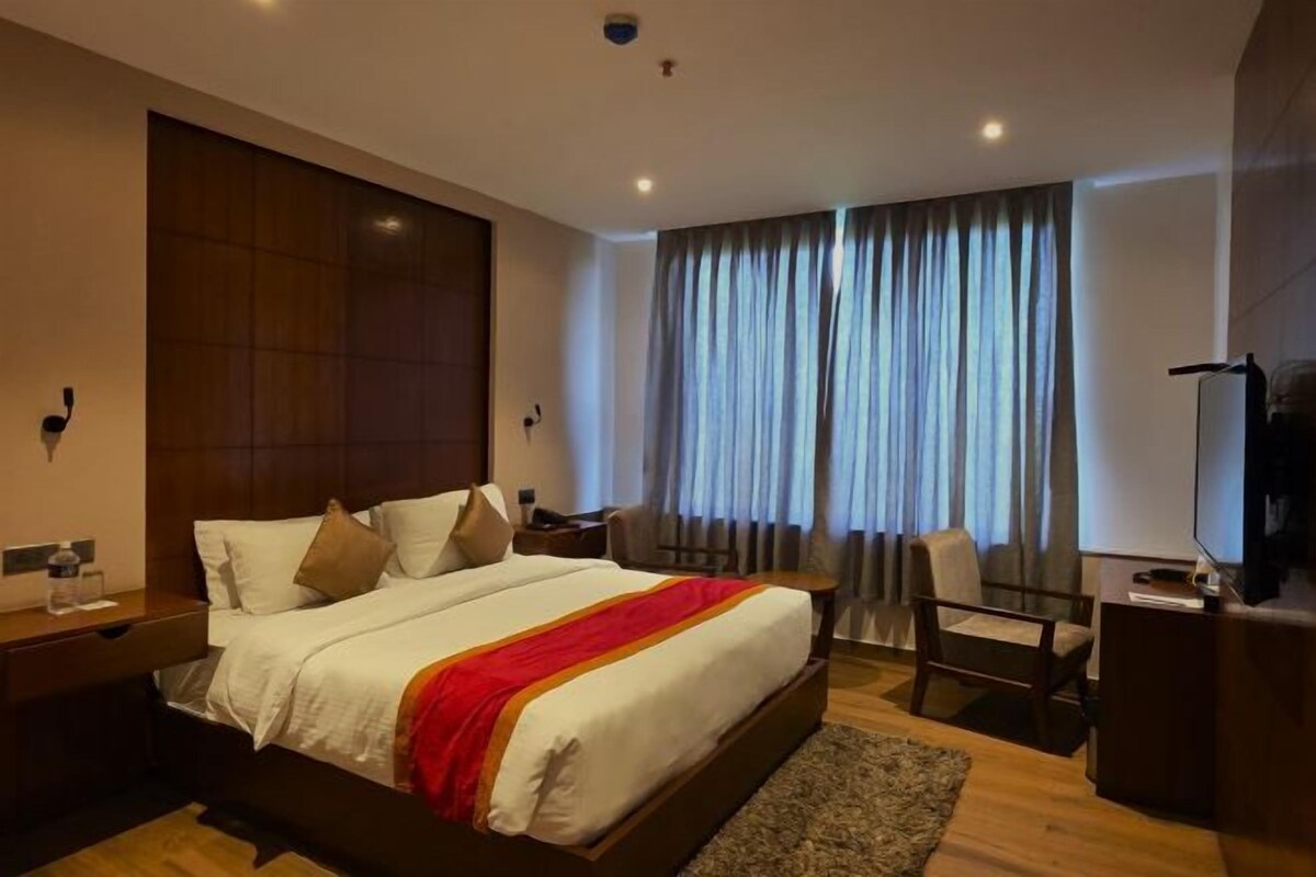 A hotel room with a large bed, a desk, a chair, and a television.