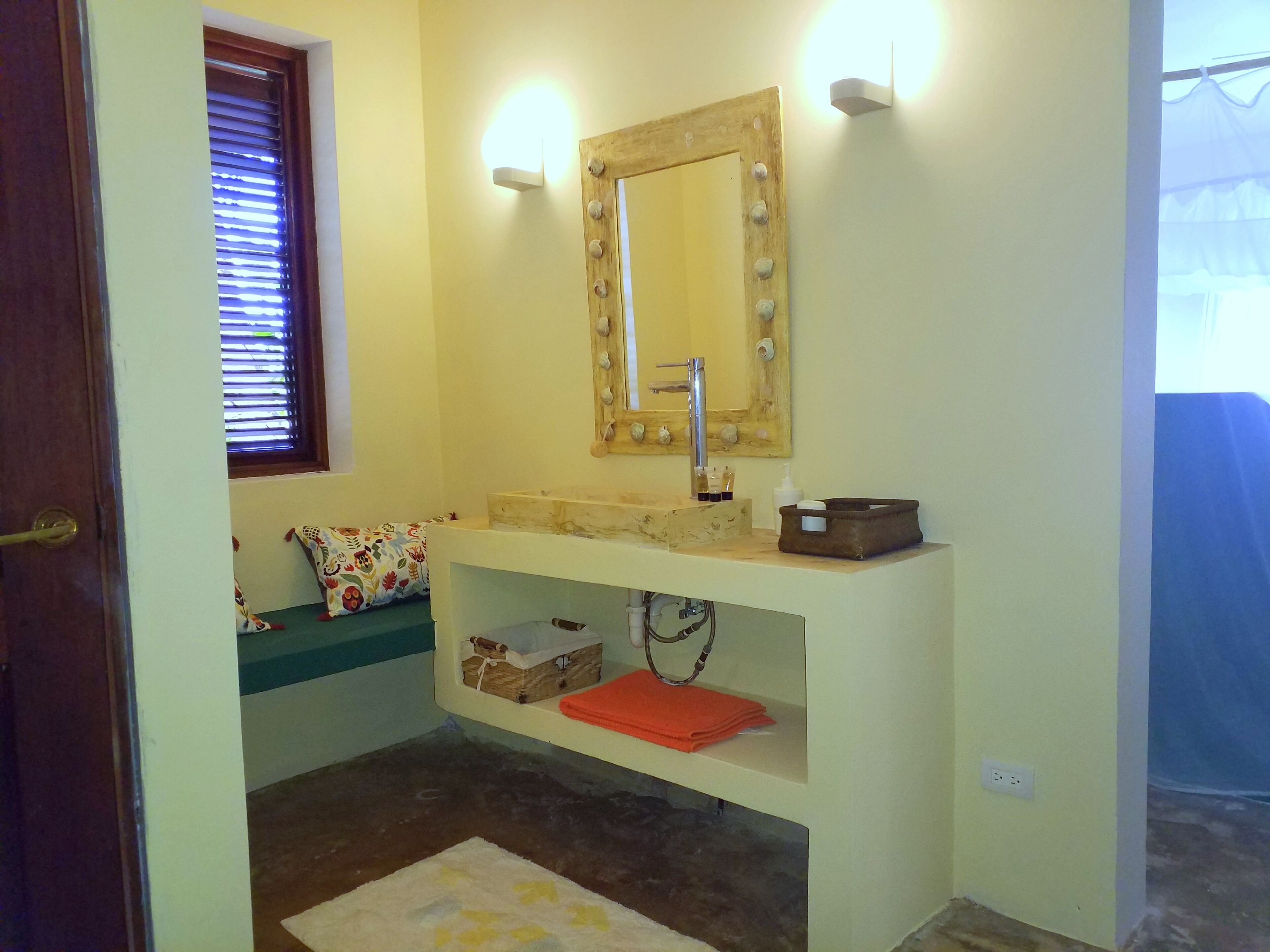 A bathroom with a wooden vanity, a mirror with lights, a sink, and a window with blinds.