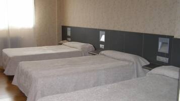 Habitación de hotel con tres camas individuales, cabecera, mesitas de noche y una ventana con cortinas.