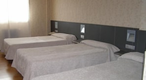 Habitación de hotel con tres camas individuales, cabecera, mesitas de noche y una ventana con cortinas.