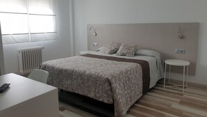 A hotel room with a bed, bedside tables, a desk, and a radiator.