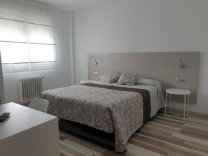 A hotel room with a bed, bedside tables, a desk, and a radiator.