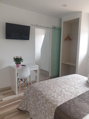 A bedroom with a bed, a desk with a chair, a television, and a wardrobe.
