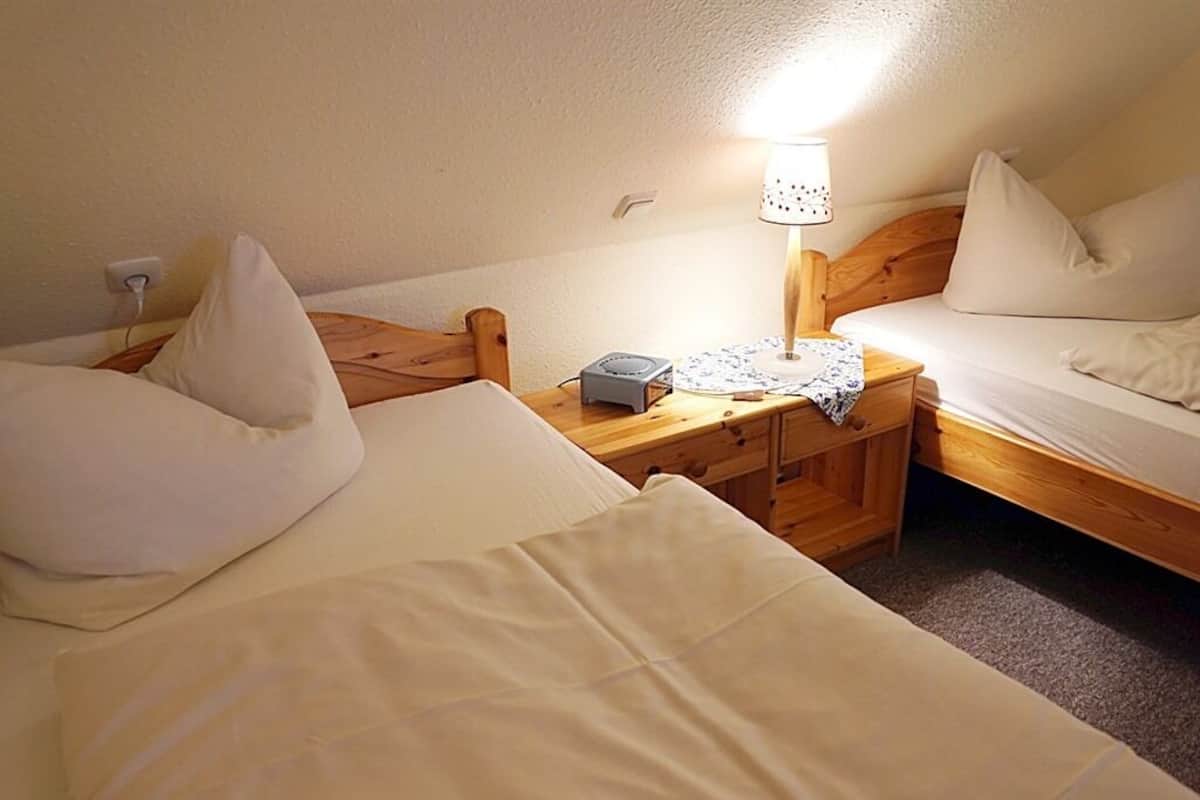 A small, cozy room with two single beds, a bedside table with a lamp, and a power outlet.
