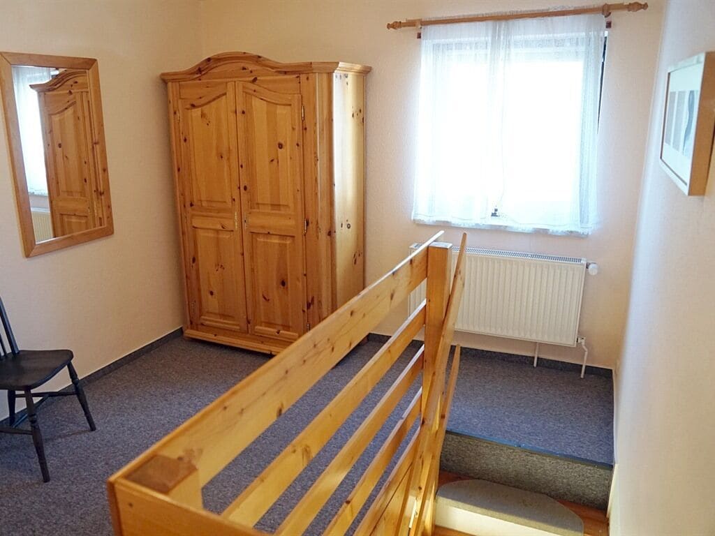 A room with a wooden bunk bed, a wardrobe, a radiator, and a window with curtains.