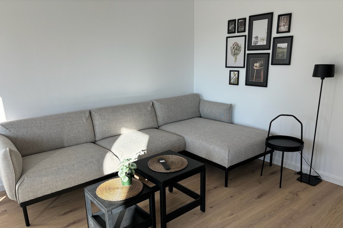 A modern living room with a grey sectional sofa, a small black table with a woven placemat, and a floor lamp.