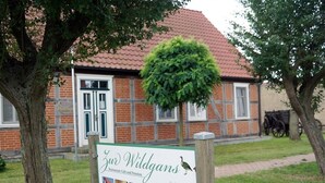 A sign for 'Zur Wildgans Restaurant, Café und Pension' with a view of a traditional brick building and a tree in the foreground. - Restaurant und Pension Zur Wildgans (Arendsee)