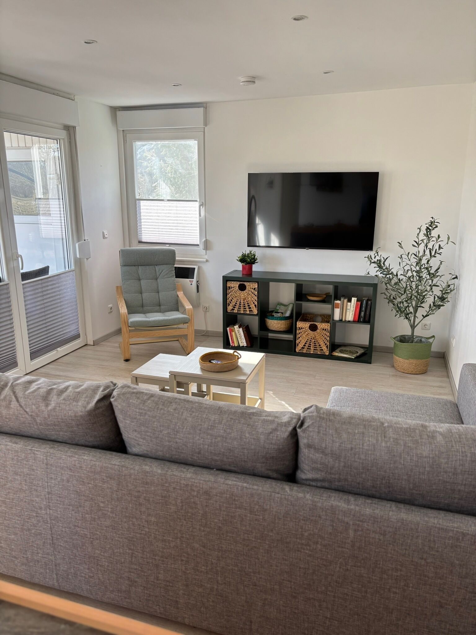 Een moderne woonkamer met een grijze bank, een houten stoel, een klein tafeltje, een televisie en een boekenplank.