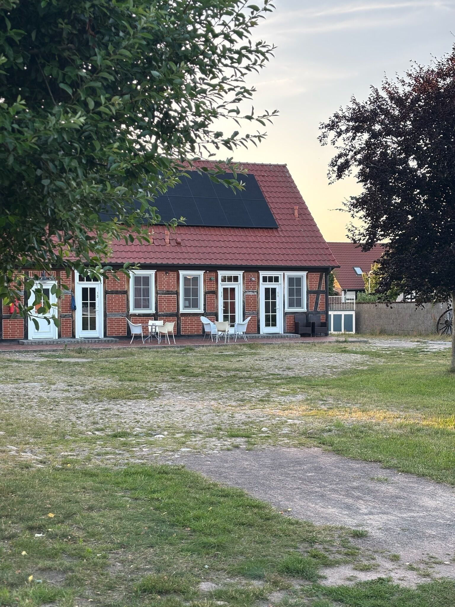 A brick building with a red roof, white-framed windows, and outdoor seating.