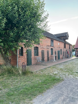 A brick building with green shutters, a paved walkway, and a grassy area.