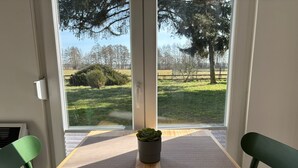 A room with a large window, a wooden table, two green chairs, and a potted plant. - Restaurant und Pension Zur Wildgans (Arendsee)
