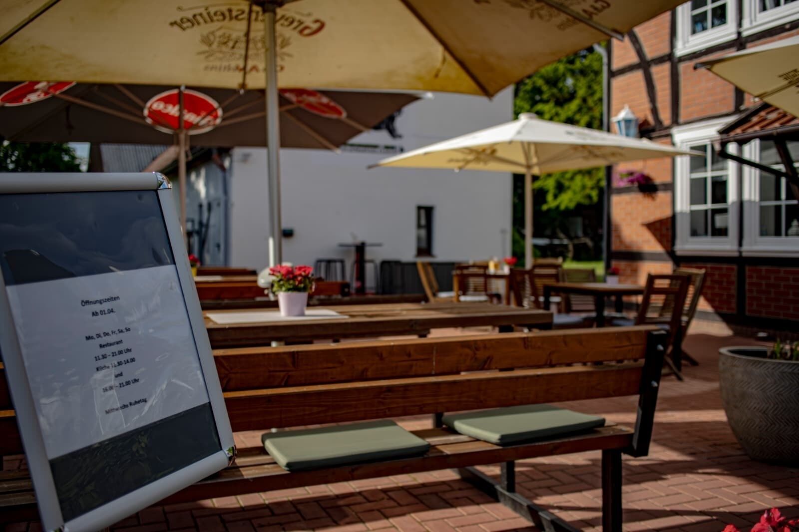 Outdoor seating with wooden benches and umbrellas, a menu board, and a brick building in the background.