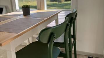 A dining area with a table and chairs, a potted plant, and a view through large windows.