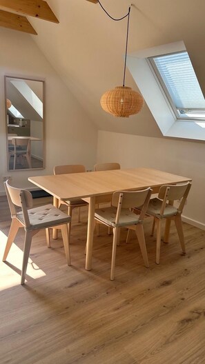 Un comedor con una mesa y sillas de madera, una lámpara colgante tejida, un tragaluz y vistas al exterior.
