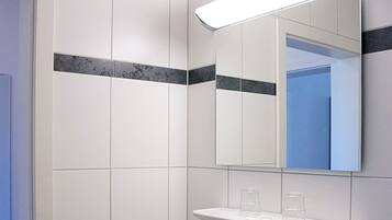 A bathroom with white tiles, a mirror, and a shelf with glasses.
