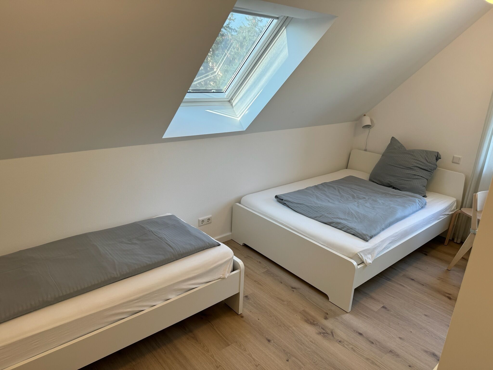 Un apartamento pequeño de una habitación con dos camas, un tragaluz y piso de madera.
