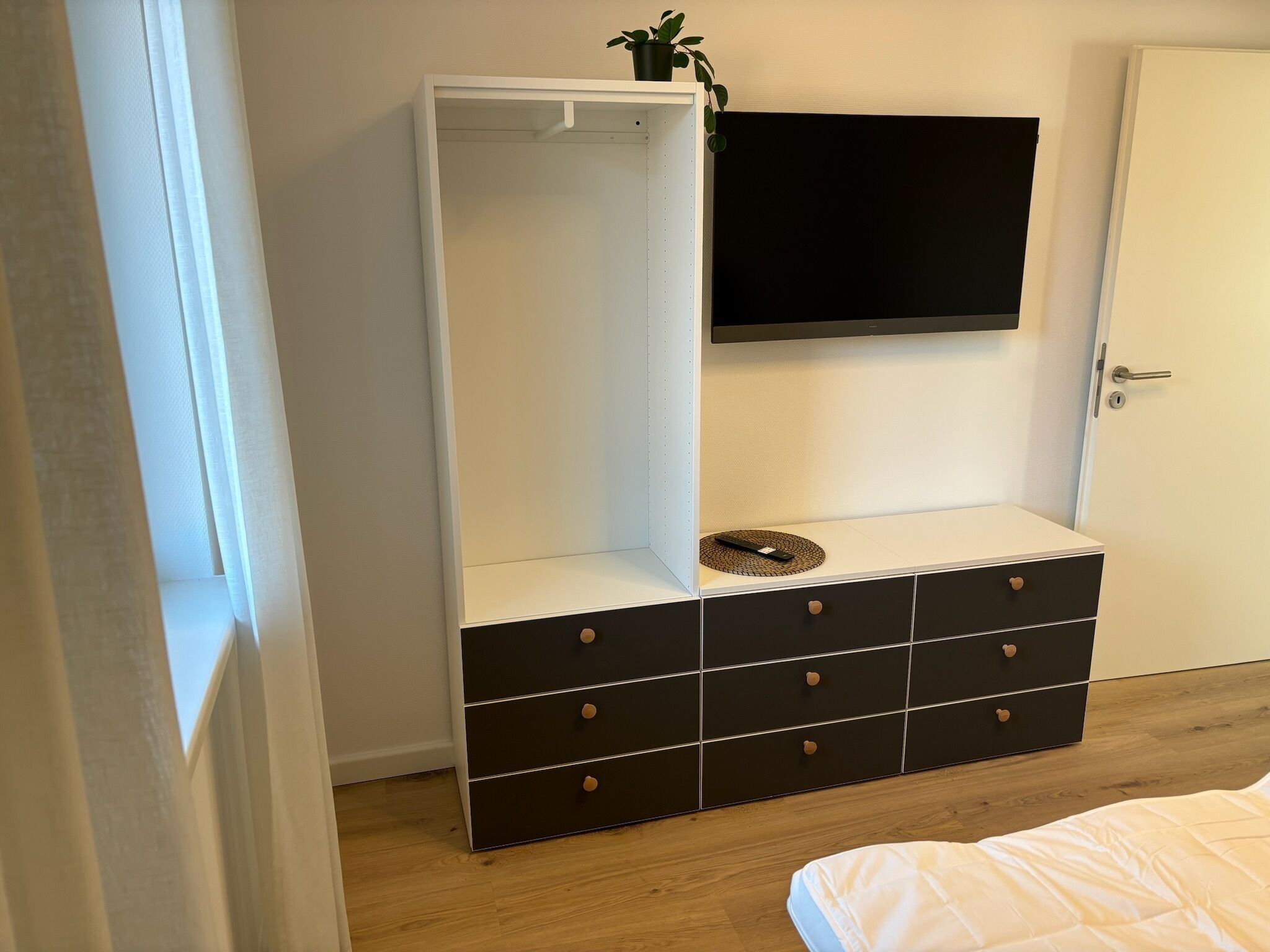 A bedroom with a bed, a wardrobe, a television, and a small plant.