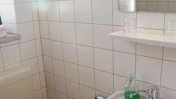 Un baño con azulejos blancos, un lavamanos con una botella verde y un espejo sobre él.