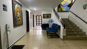 Un pasillo con dispensador de agua, un sofá azul y una escalera.