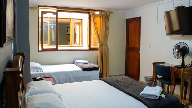 Habitación de hotel con dos camas, un escritorio con silla, televisión y ventana con cortinas.