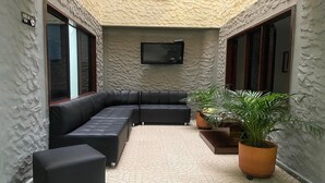 Un interior moderno con un sofá de cuero negro, un televisor de pantalla plana en la pared y plantas en macetas.