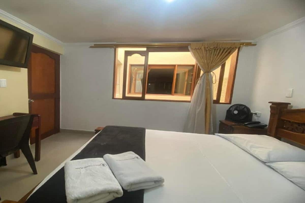 Ein Hotelzimmer mit Bett, Schreibtisch, Stuhl, Wandfernseher und einem fenster mit Vorhängen.