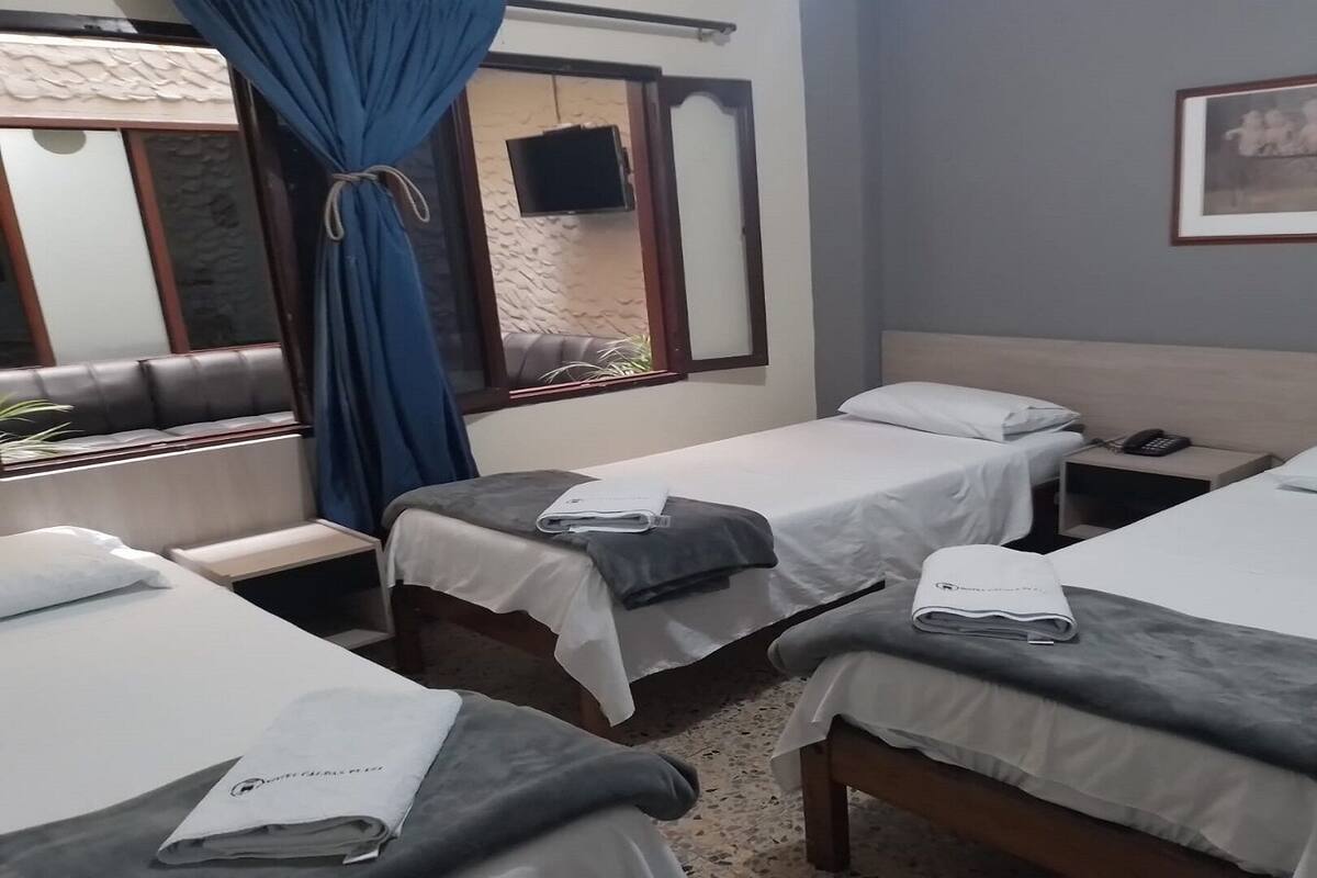 Ein Hotelzimmer mit zwei Einzelbetten, einem kleinen Nachttischchen mit Telefon, einem Fenster mit Vorhängen, einem am Wand montierten Fernseher und einem gerahmten Bild.