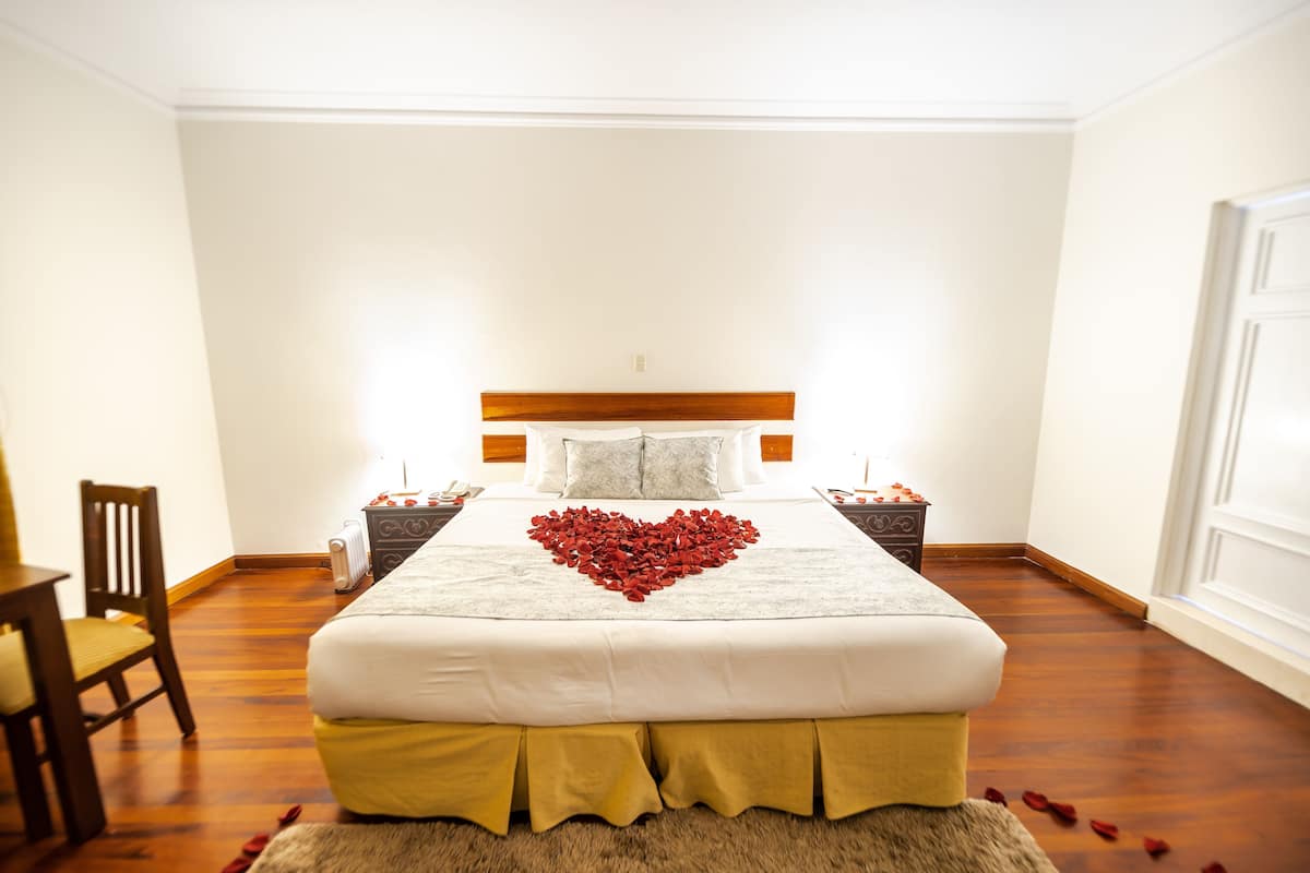 A neatly made bed with a heart-shaped rose arrangement, a wooden headboard, and a wooden floor.