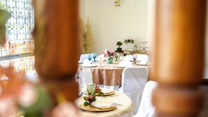 Uma sala de jantar com mesa posta para refeição, um candelabro e uma janela com grades de ferro decorativas.