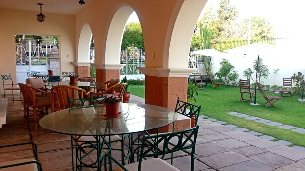 Uma área de pátio coberta com mesa e cadeiras de vidro, cercada por arcos e plantas em vasos.