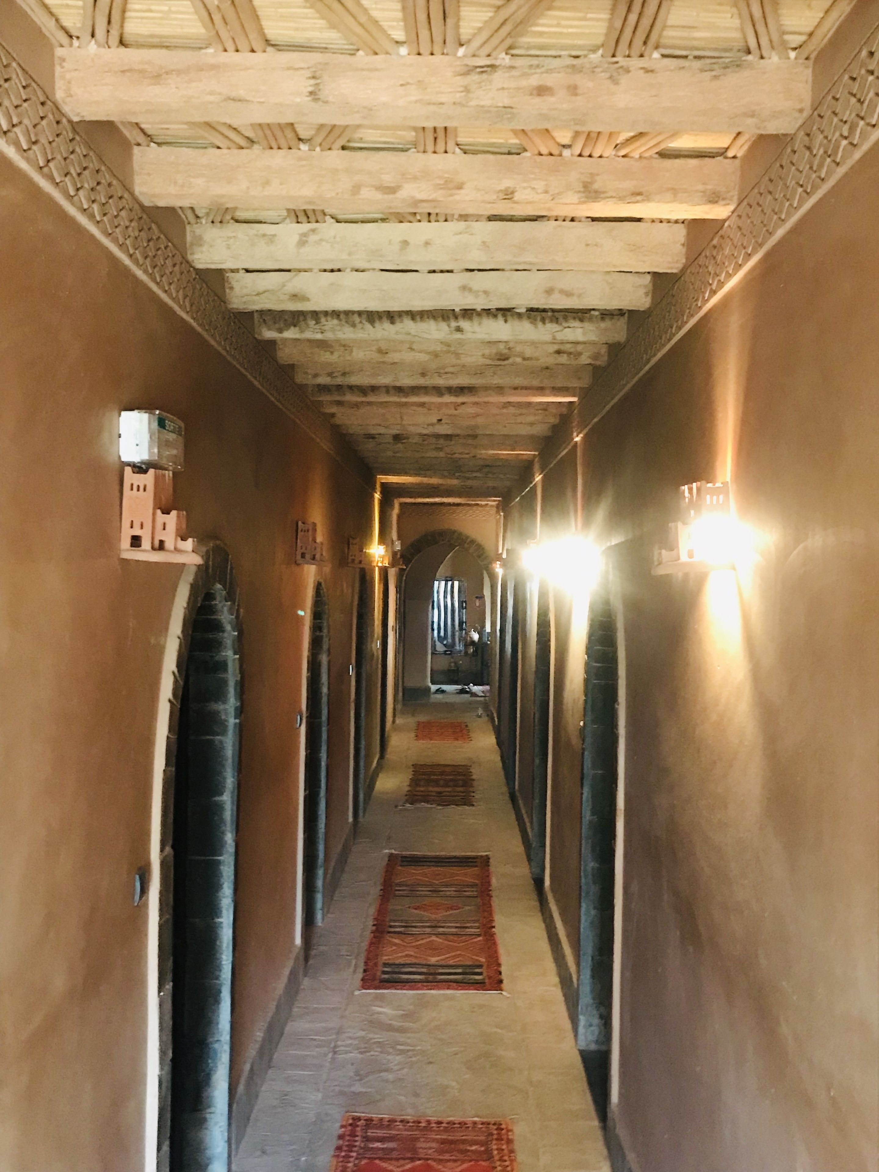 Ein Korridor mit Holzbalken an der Decke, einem gemusterten Teppich und Wandleuchten.