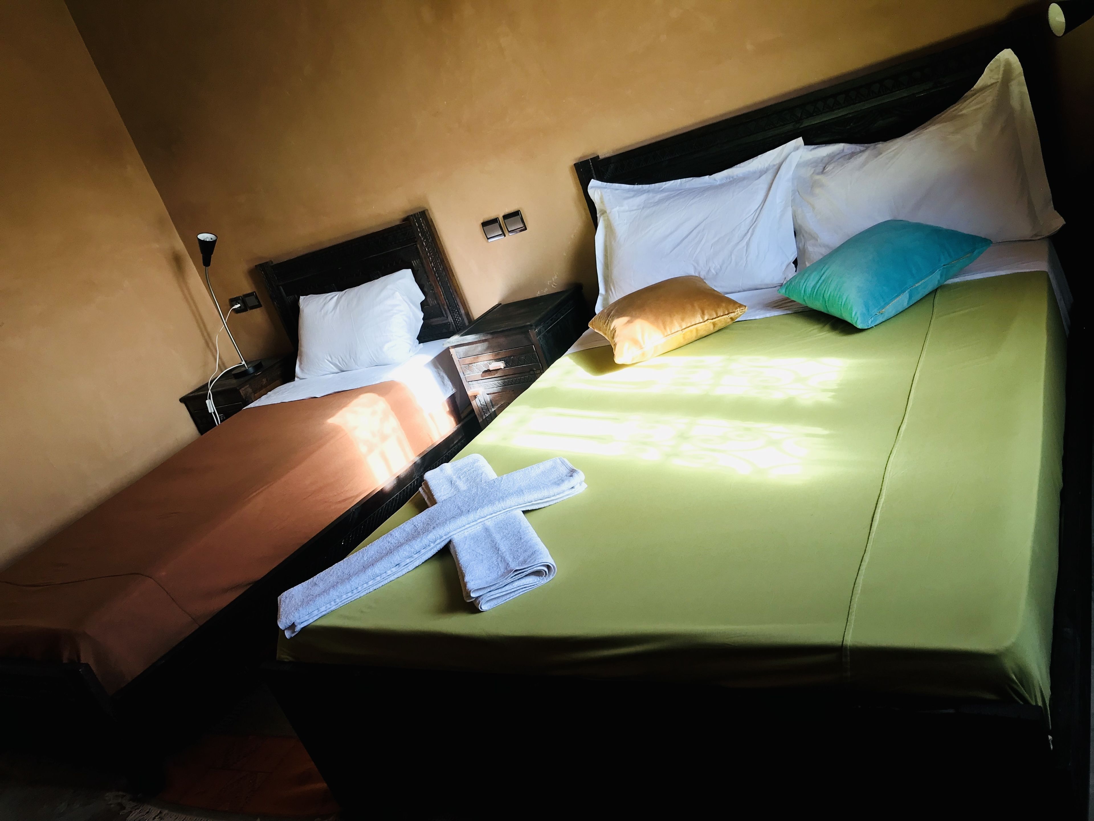A bed with a green sheet, white pillows, and a blue pillow. There is a towel on the bed.