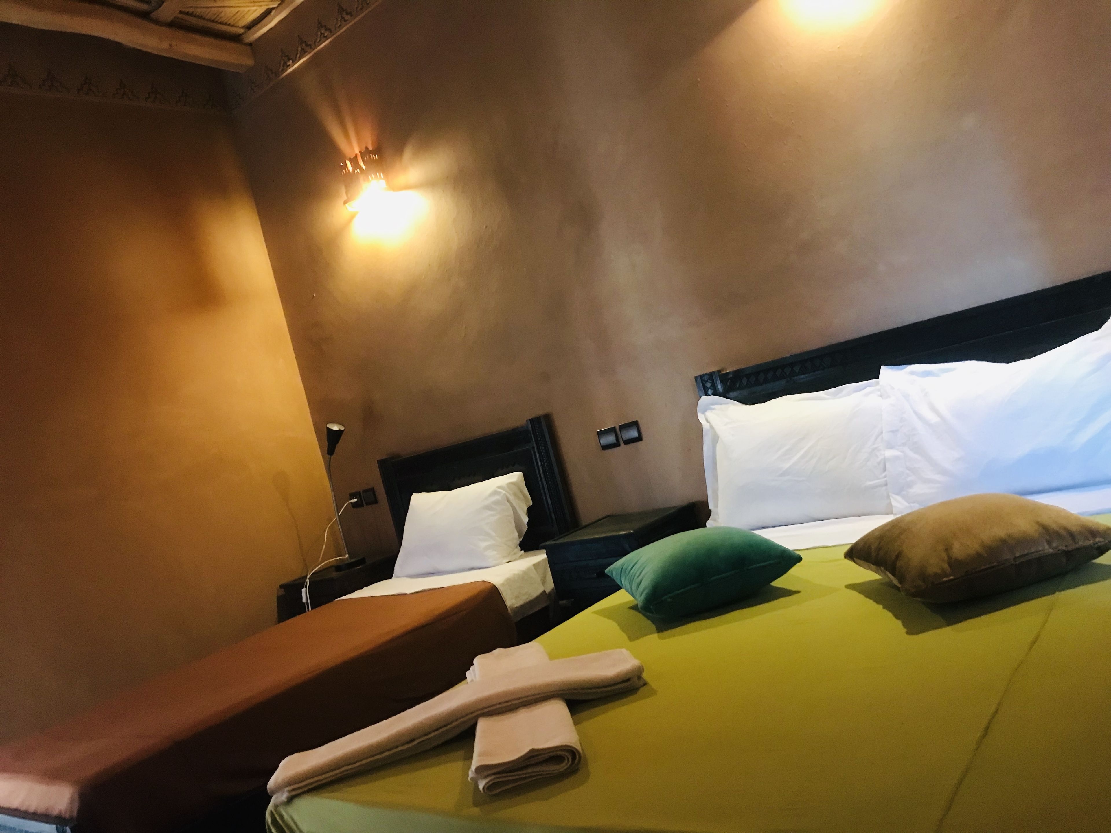 Una camera d'albergo con un letto, cuscini, una panca e un lampadario a parete.