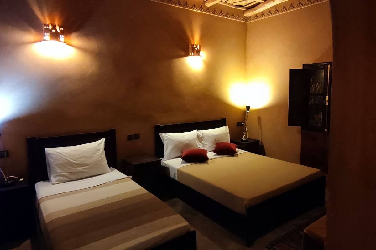 A hotel room with two beds, each with a headboard, bedside tables, and wall-mounted lamps.