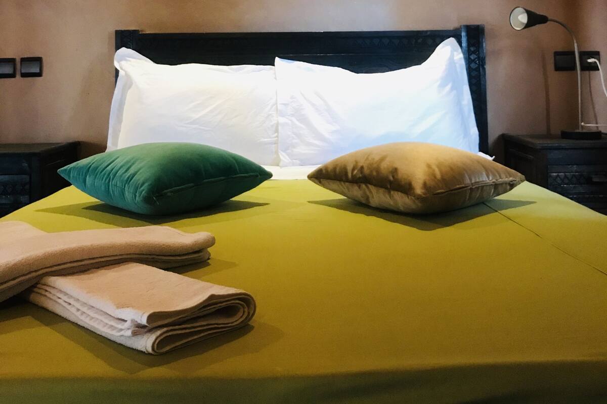 A neatly made bed with a green and yellow bedspread, two pillows, and a folded towel.