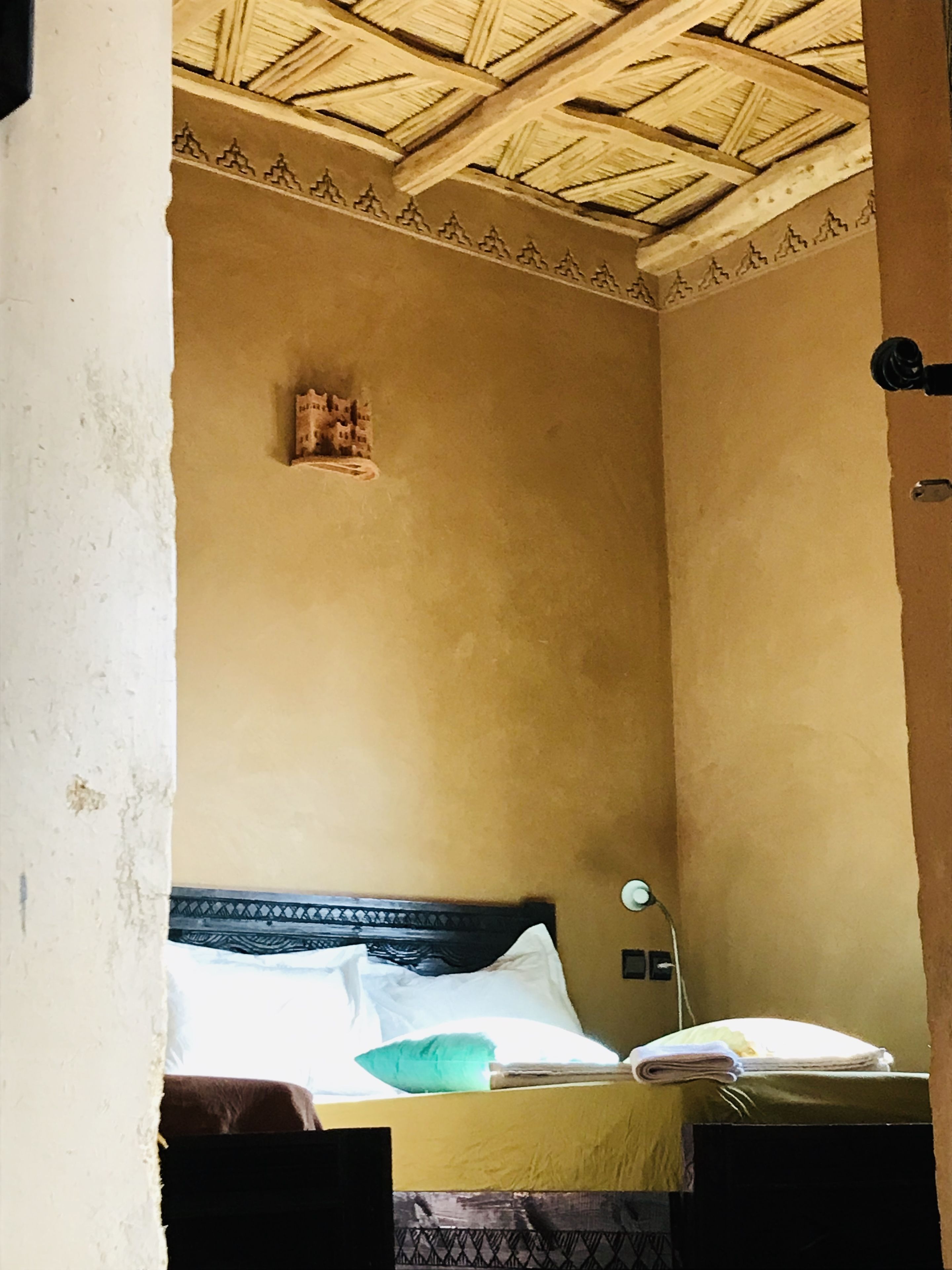 Una habitación con una cama, una lámpara fijada a la pared y un techo decorado.