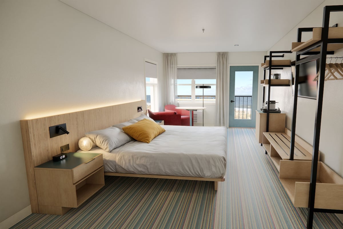 Habitación de hotel moderna con cama, mesitas de noche, escritorio, silla, armario y vista al mar.