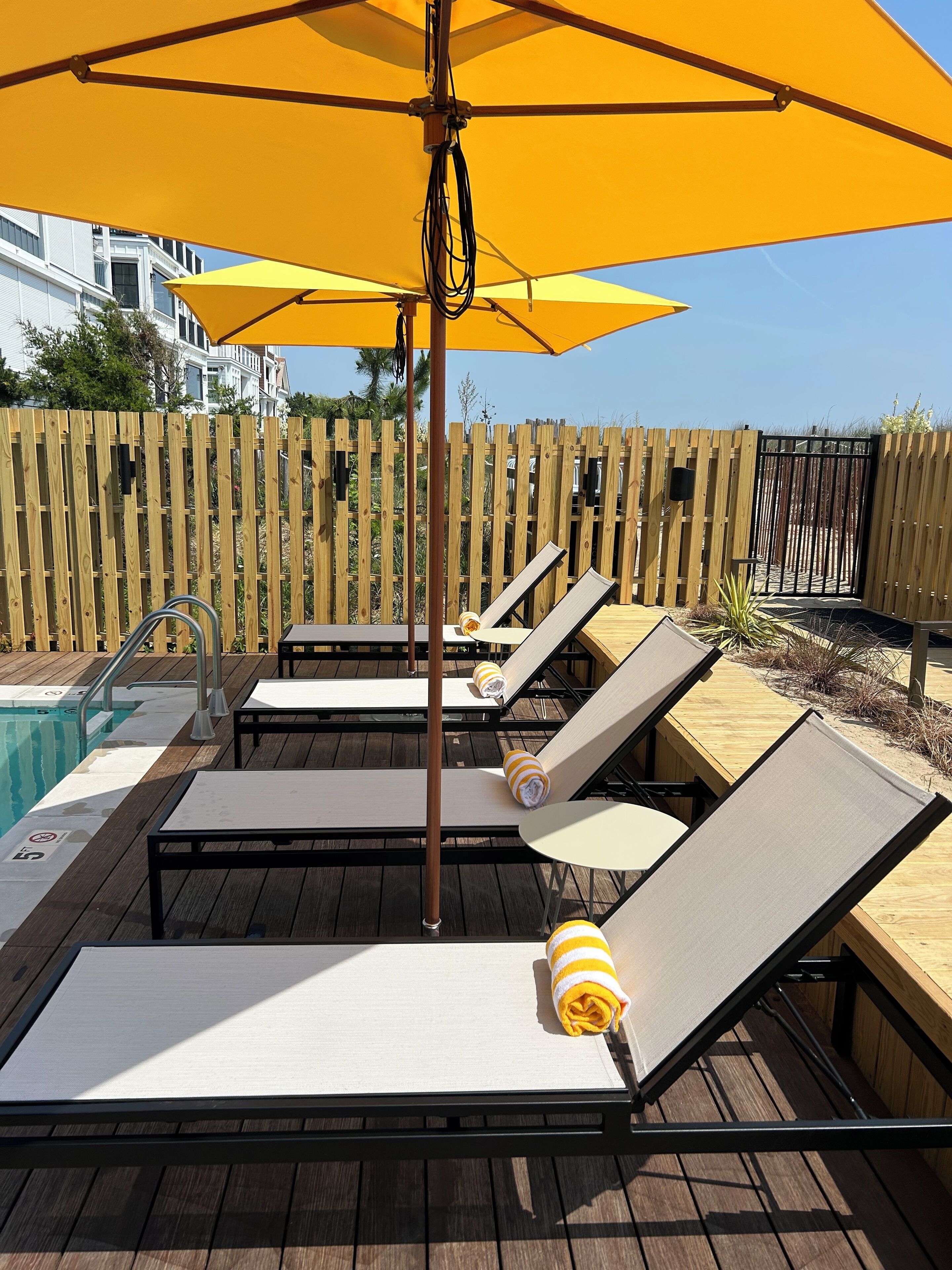 A poolside area with wooden deck, lounge chairs, and a yellow umbrella.