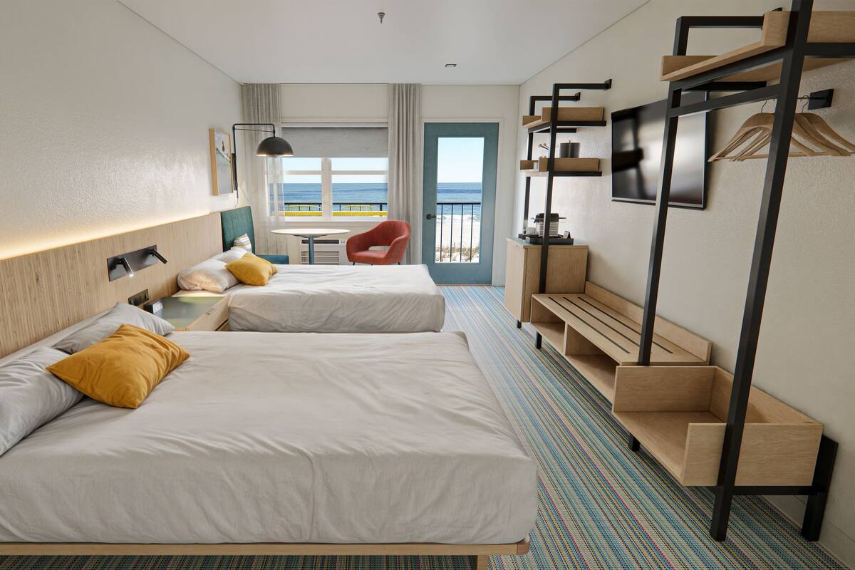 Habitación de hotel con dos camas, una silla, un escritorio, vista al mar y un balcón.
