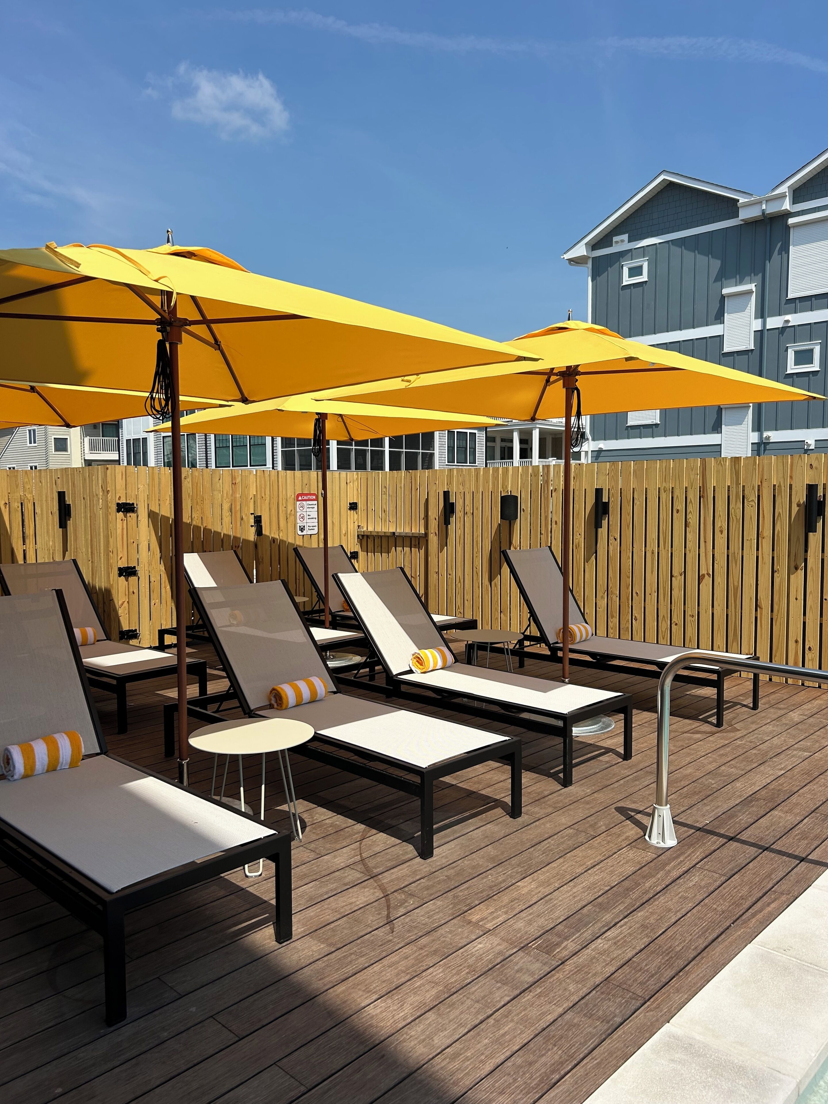 Une terrasse avec des chaises longues et des parasols jaunes, une clôture en bois et un bâtiment en arrière-plan.