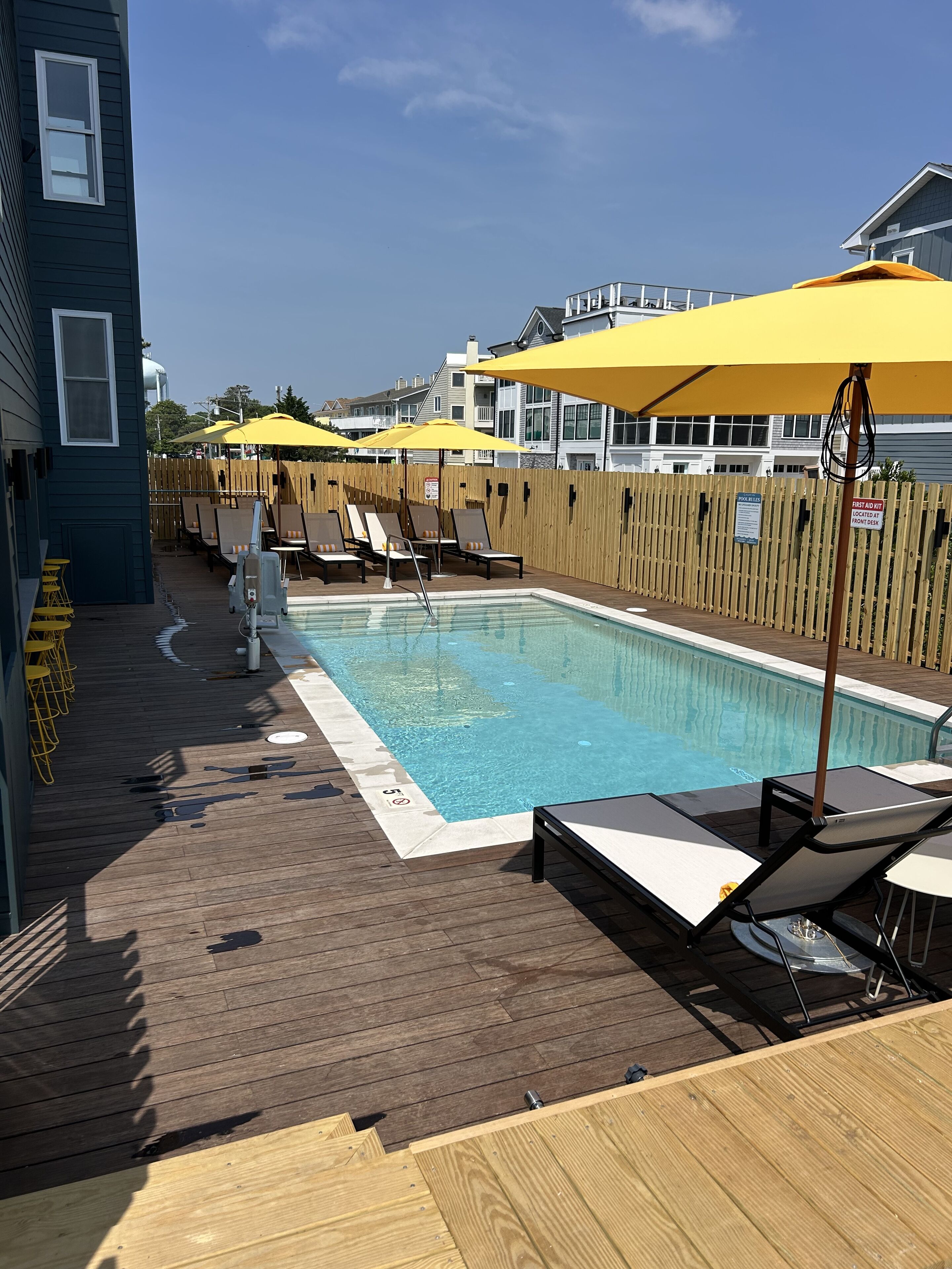 Un espace piscine avec des chaises longues et des parasols jaunes, une terrasse en bois et une clôture en bois.
