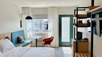 A hotel room with a bed, a desk, a chair, a window with a view, and a bunk bed.